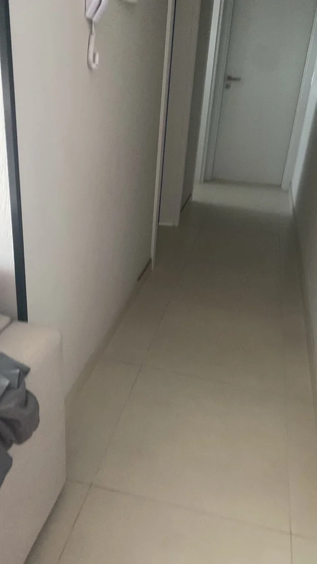 Corredor interno com paredes claras, portas e piso claro.