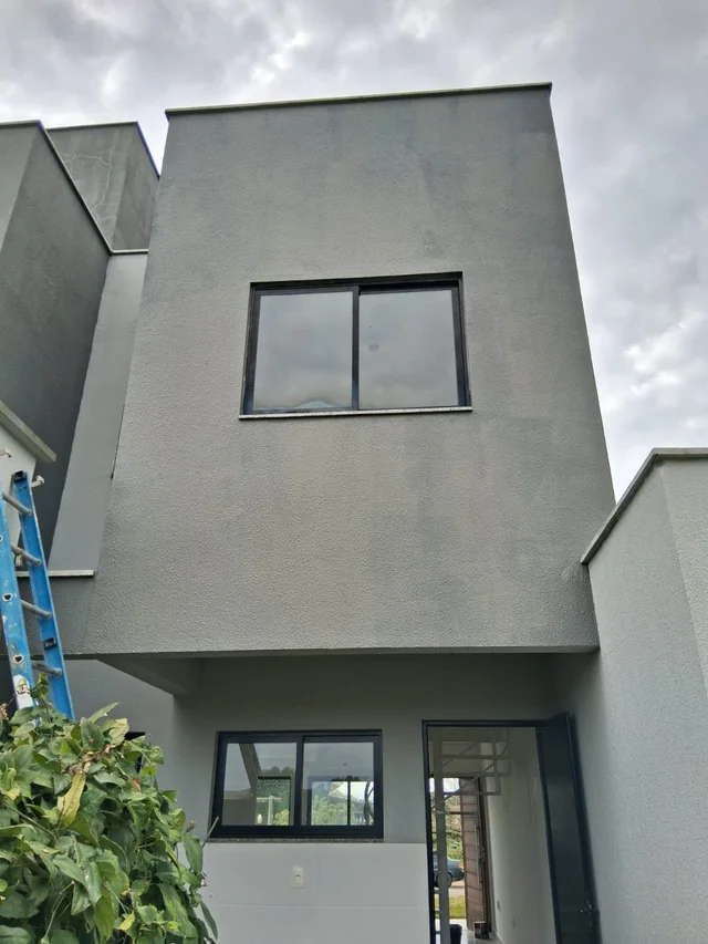 Fachada cinza de uma residência com janela e entrada.