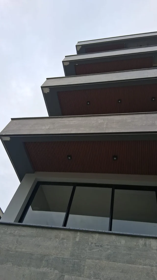 Edifício visto de baixo, com varandas, fachada cinza e detalhes em marrom.